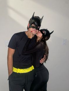 a man and woman dressed up as batman kissing each other's forehead while posing for the camera