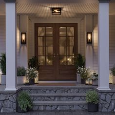 the front entrance to a house with potted plants on the steps and lit up by lights