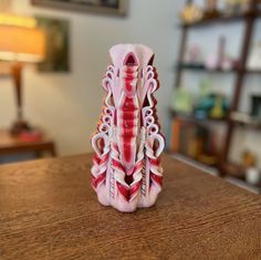 a pink and white vase sitting on top of a wooden table next to a lamp