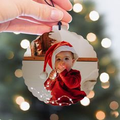 a hand holding a christmas ornament with a small child in a santa hat