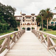 a wooden bridge crossing over a body of water in front of a large house with palm trees