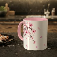 a pink and white coffee mug sitting on top of a counter next to some cookies