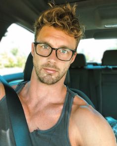 a man with glasses sitting in the back seat of a car looking at the camera