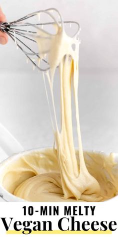 a hand holding a whisk over a bowl filled with vegan cheese sauce