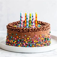 a chocolate birthday cake with lit candles on it and sprinkles around the edges