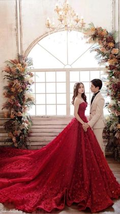 a man and woman standing next to each other in front of a window wearing red dresses