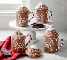 four gingerbread mugs decorated with white icing and candy canes on a cake stand