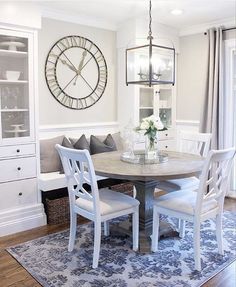 a dining room table with white chairs and a large clock on the wall above it