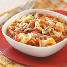 a white bowl filled with pasta and meat on top of a red plate next to a fork