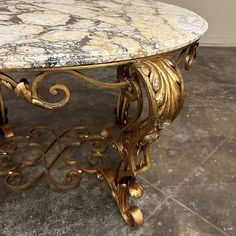 a marble top coffee table with gold leaf designs on the legs and bottom, sitting on a tile floor