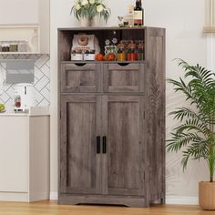 a wooden cabinet sitting in the middle of a kitchen next to a potted plant