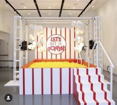 a stage set up for an event with red and white stripes on the walls, yellow popcorn buckets in front of it