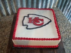 a cake decorated with the kansas chiefs logo on top of a wooden table in front of a corrugated wall