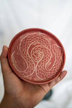 a hand holding a red and white bowl with designs on it's sides, in front of a white background