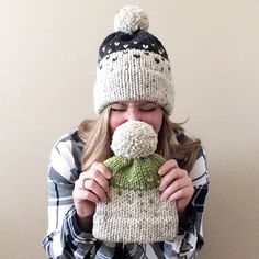 a woman wearing a knitted hat and scarf covers her mouth with a pom - pom