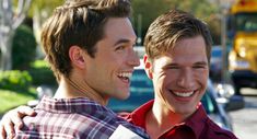 two young men standing next to each other in front of a school bus and smiling