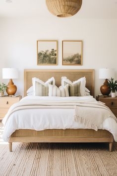 a bed with white linens and pillows in a large room next to two pictures on the wall