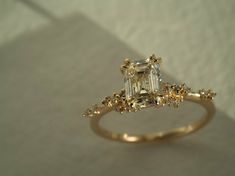 a fancy ring with an emerald cut diamond surrounded by small yellow and white flowers on the band