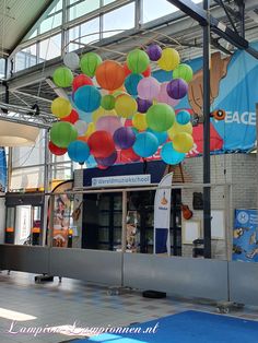 there are many different colored balloons hanging from the ceiling in front of an entrance to a building