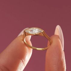 a woman's hand holding a gold ring with a pear shaped diamond