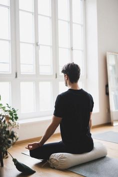 a man sitting on the floor in front of a window doing yoga with his feet up