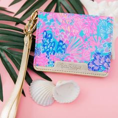 a pink and blue wallet sitting on top of a palm leaf next to a shell