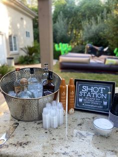 an outdoor bar with bottles and drinks on the table next to a sign that says shot station