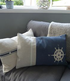 three pillows are sitting on a couch in front of a window with a ship wheel