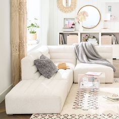 a living room with a large white sectional couch and pillows on the floor in front of a round mirror