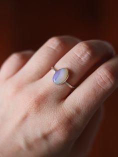 This dainty and extremely delicate ring features a beautiful Australian Lightning Ridge opal, set in a fine silver bezel with open back. The band is made with a sterling silver square wire. Size 6Handmade It's a perfect everyday ring - simple, yet full of character. Can be stacked and combined with other rings or worn by itself, for a more minimalist look. Delicate purples make each opal absolutely unique, with its own stunning colours and inclusions. The look of the gemstone changes in differen Delicate Silver Opal Ring In Sterling Silver, Minimalist Adjustable Opal Ring, Minimalist Adjustable Opal Open Ring, Sterling Silver Opal Ring With Bezel Setting As Gift, Dainty Stackable Sterling Silver Opal Ring, Gift Opal Ring With Bezel Setting In Sterling Silver, Minimalist Opal Rings With Gemstone, Adjustable Minimalist Moonstone Ring In Sterling Silver, Minimalist Oval Opal Ring For Gift