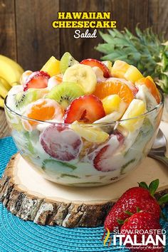 a fruit salad in a glass bowl on top of a wooden table next to pineapples