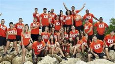 a group of people in orange shirts posing for a photo on rocks with their hands up