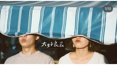 two people standing under a blue and white awning with their faces covered by pillows