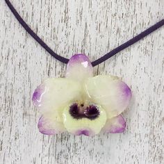 A real Dendrobium Orchid preserved in resin is showcased in this pendant necklace presented by Danai of Thailand. The orchid has pale yellow petals tipped in purple and hangs from a deep purple leather cord. Two sliding tiger's eye beads dyed purple secure the ends of the cord and allow the necklace length to be adjusted. Dendrobium Orchid, Gifts For Travelers, Orchid Necklace, Orchid Jewelry, Yellow Petals, The Orchid, Yellow And Purple, Purple Orchids, Dope Jewelry