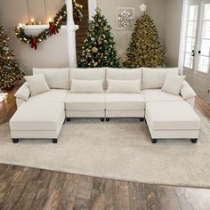 a white sectional couch sitting on top of a hard wood floor next to christmas trees