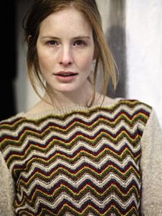 a woman with brown hair wearing a multicolored knit sweater and looking at the camera