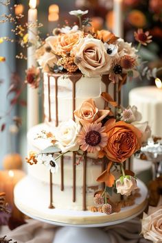 a three tiered wedding cake with flowers on top and candles in the back ground