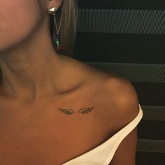 a woman's chest with an angel wing tattoo on the left side of her neck