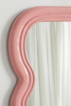 a pink mirror hanging on the wall next to a curtain