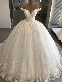 a white wedding dress with flowers on the skirt and off the shoulder, is displayed in front of a mirror