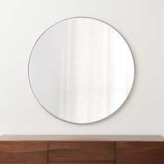 a round mirror sitting on top of a wooden dresser next to a wall mounted shelf