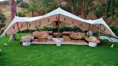 a large tent set up with couches and tables in the middle of a grassy area