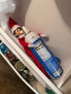 an elf is in the bottom shelf of a refrigerator holding a can of paint and a toothbrush