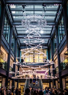 people are standing in the middle of a building with an artistic light sculpture hanging from it's ceiling