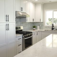 a kitchen with white cabinets and marble counter tops