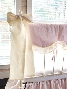 a crib with pink and white ruffled bedding in front of a window