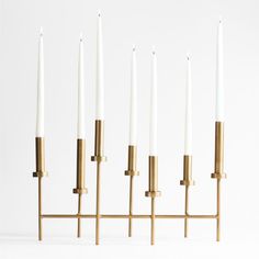 five white candles are lined up in a row on a brass stand with four smaller ones