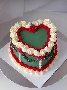 a heart - shaped cake with white frosting and red flowers on top is being held by someone's hand