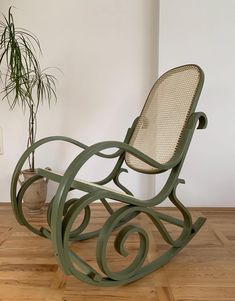 a rocking chair sitting on top of a hard wood floor next to a potted plant