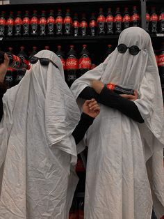 two people dressed in ghost costumes standing next to each other with soda bottles behind them